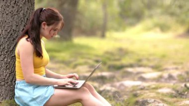 Genç bir kadın parkta dizüstü bilgisayarla ders çalışıyor. Okul uzaklığı eğitim üniversitesine.