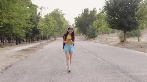Kaukasische Frau auf dem Campus der Universität, hört Musik mit Kopfhörern im Smartphone — Stockvideo