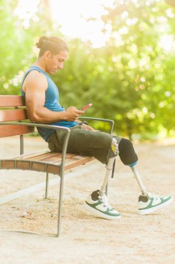 Parktaki bankta oturan engelli bir adam akıllı telefon kullanıyor. Kapsama, teknoloji ve adaptif yaşam tarzı kavramı