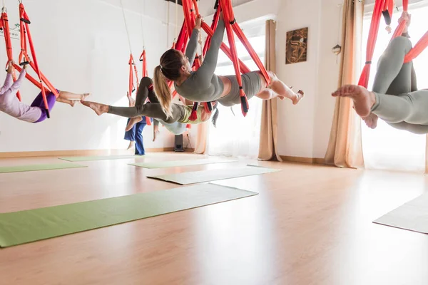 Çok kültürlü bir gruptaki kadınlar, vinyasa kursu sırasında kumaş hamaklarda asılı halde havadan yoga egzersizleri yapıyorlar.