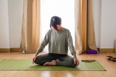 İspanyol kadın yoga pozunda oturuyor, Vinyasa yogası yapmadan önce nazikçe boynunu esnetiyor. Farkındalık ve sağlığa odaklanmak