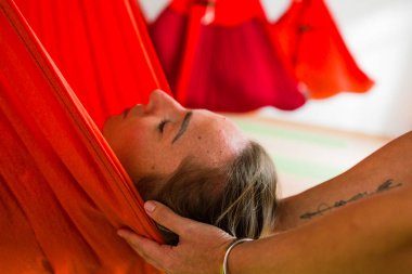 Kadın, turuncu bir yoga hamağında dinlenirken kafa desteği alıyor. Huzur ve rahatlama arıyor.