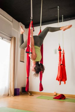 Havadan yoga hamağında akrobasi ve vinyasa yapan bir kadın stüdyoda vücudunu baş aşağı geriyor.