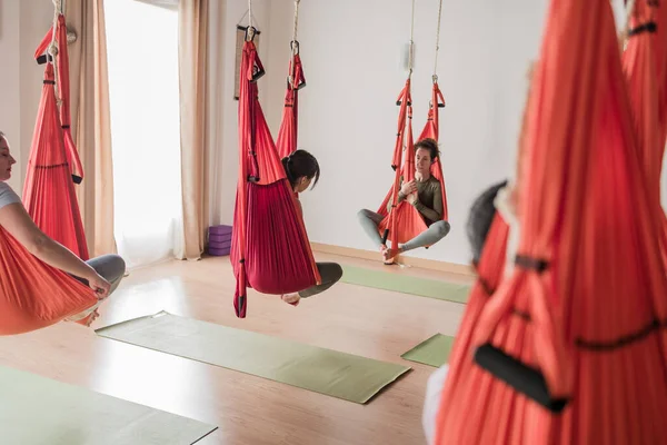 Yerçekimi karşıtı vinyasa yoga dersinden zevk alan çok kültürlü bir grup kadın stüdyo hamaklarında denge ve rahatlama buluyor.