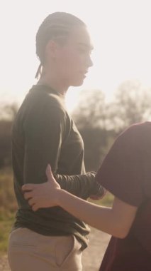 Genç lezbiyen çift, güzel bir günbatımında parkta romantik bir anın tadını çıkarırken neşeyle kucaklaşıp gülüyorlar.