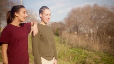 Parkta yürüyüş yapan mutlu lezbiyen çift. Romantik bir günbatımında kucaklaşan iki genç kadın konuşuyor ve gülüyor.