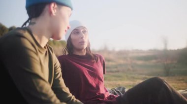 İki genç lezbiyen kız arkadaş çimlerin üzerinde oturuyor, konuşuyor ve birlikte gülüyorlar. Mutlu kadınlar gün batımında romantik bir buluşmanın keyfini çıkarıyorlar.