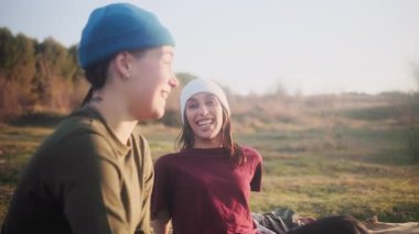 Genç lezbiyen çift dışarıda birlikte vakit geçiriyorlar. Çimlerin üzerinde oturuyorlar, konuşuyorlar ve gülüyorlar altın saat günbatımında