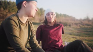 Çimlerin üzerinde oturan, konuşan ve birlikte gülen genç lezbiyen çift. Açık havada aynı cinsiyetten bir çiftin mutlu samimi anları.