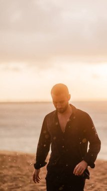 Genç adam gün batımında kumlu bir sahilde yürüyor, hayatı düşünüyor ve huzurlu, doğal bir çevrede özgürlüğü kucaklıyor.