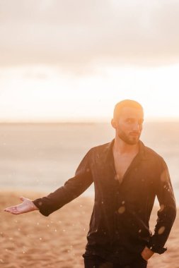 Gün batımında plajda duran ıslak tişörtlü genç adam anı hisseder ve yeni hayaller için ilham kaynağı bulur.