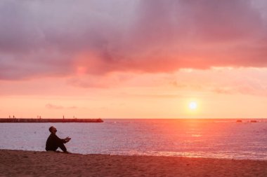 Genç adam, okyanusun üzerinde canlı bir günbatımında plajda huzur ve derin ilhamın tadını çıkarıyor.