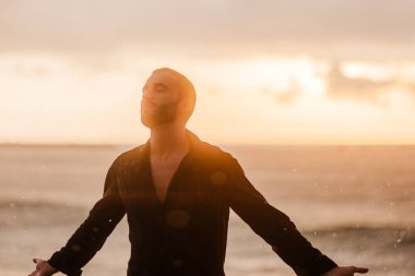 Suda duran genç adam, gözleri kapalı, kolları açık, altın saat boyunca ilham ve hoşnutluk hissediyordu.