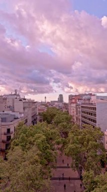 Barcelona 'daki Rambla de Catalunya' nın üzerinden geriye doğru uçan hava manzarası çarpıcı mor ve pembe bulutlu günbatımında