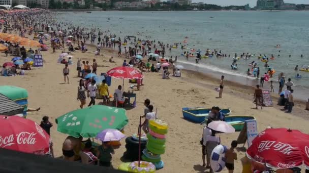 Um monte de pessoas na praia de areia de banho lotada. As pessoas nadam no mar, Qingd da China — Vídeo de Stock