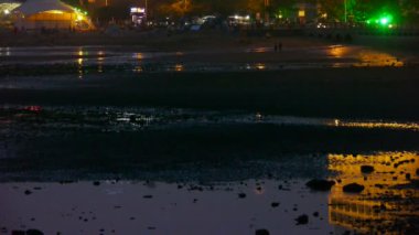 Neon House yansıması körfezde. Araba kıyıda seyahat ediyor. Turistler kum beac 'te oynuyor.