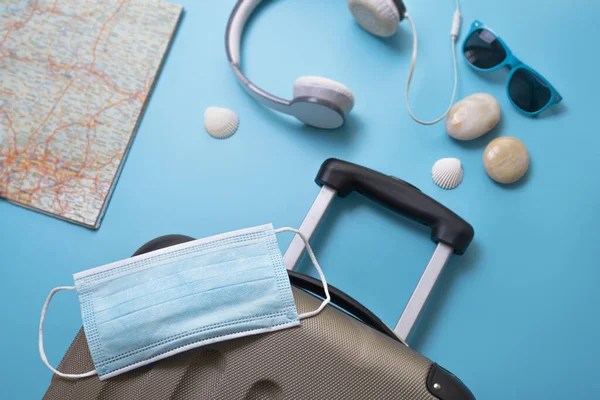 Reisen während der Zeit von COVID-19. Medizinische Maske, Koffer, Sonnenbrille, Karte, Muscheln auf blauem Hintergrund. Urlaub, Urlaub in Corona-Zeiten. — Stockfoto