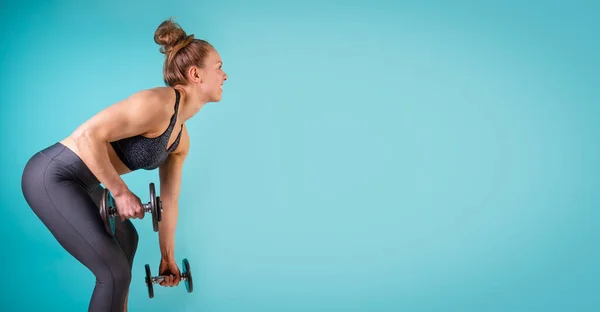 青い背景にダンベルで働くフィットネスガールの写真。体育の女性は腕の運動をする。強さと動機、スポーツと健康的なライフスタイル。テキストやロゴのためのフリースペース,コピー — ストック写真