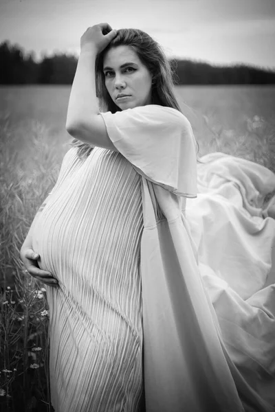 Junge schwangere Frau mit langen Haaren und Kleid in der Natur. Mutterschaft. Schwarz-Weiß-Foto. — Stockfoto