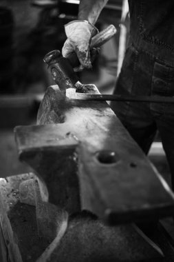 Demirhanede el yapımı metal ürünlerinin üretim sürecindeki demirci. Demirci çekiçle metal dövüyor. Siyah beyaz fotoğraf