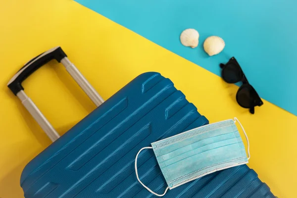 Reisen während der Zeit von COVID-19. Medizinische Maske, Koffer, Sonnenbrille, Muscheln auf gelbem Hintergrund. Urlaub, Urlaub in Corona-Zeiten. — Stockfoto