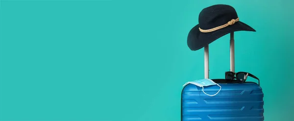 Reisen während der Zeit von COVID-19. Blauer Koffer mit medizinischer Maske, Sonnenbrille und Hut auf blauem Hintergrund. Freier Speicherplatz für Textkopien. Urlaub, Urlaub in Corona-Zeiten. — Stockfoto