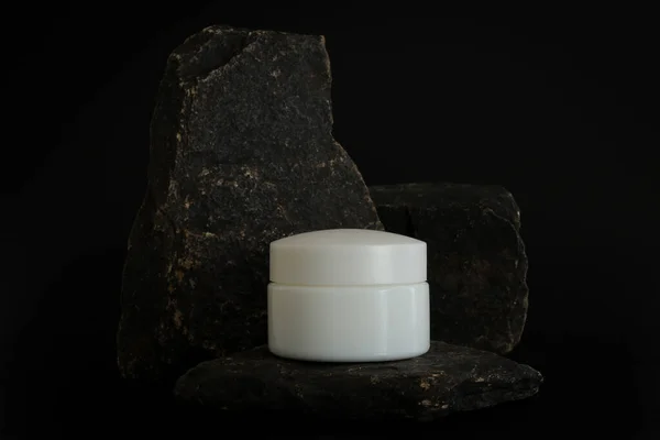 Немаркированная упаковка натурального косметического крема стоит на каменном подиуме. Крем-презентация на черном фоне. Макет. Трендовая концепция в природных материалах. Естественная косметика, кожа. — стоковое фото
