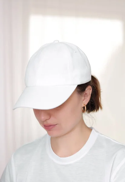 Female model wearing a white baseball cap. White cap mockup, template for picture, text or logo. Girl holding visor of cap. Free space, copy space.