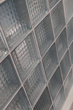 Geometrik desenli cam bloklardan oluşan bir duvar ışığı yansıtır ve dokuyu ekler, benzersiz tasarımıyla çağdaş bir alan oluşturur..