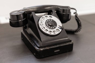 Klasik bir siyah döner telefon pürüzsüz bir ahşap masada oturur. Tasarım dairesel çevirme numaraları ve sarmal bir kablo sergiliyor, modern uzaya nostaljik bir his katıyor..