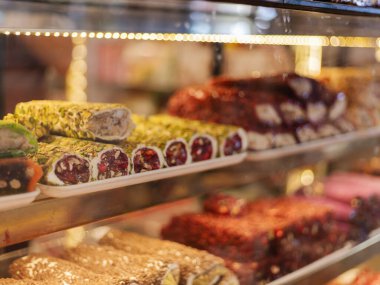 Raflar, canlı renkler ve dokuların yer aldığı geleneksel şekerlerle dolu. Ekranda fındık ve meyvelerle süslenmiş yuvarlak tatlılar, cazip müşteriler var..