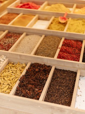 Parlak renkli baharatlar bir market tezgahındaki ahşap tepsilerde düzgünce düzenlenir. Değişik dokular ve aromalar içeren canlı seçimler dikkat çekiyor..