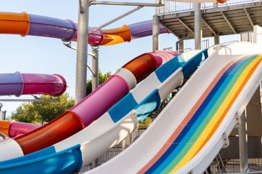 Parlak renkli su kayakları bir lunaparkta mavi gökyüzünün arka planına karşı duruyor. Aileler ve çocuklar sıcak bir günde eğlenceli aktivitelerin tadını çıkarırlar..