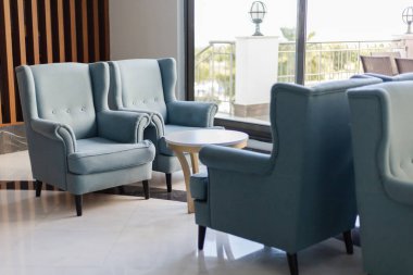 İki şık mavi koltuk, küçük yuvarlak bir masanın yanında oturur ve rahat bir oturma alanı oluşturur. Geniş pencereler doğal ışık girmesini sağlar, modern dekorun gelişmesini sağlar..