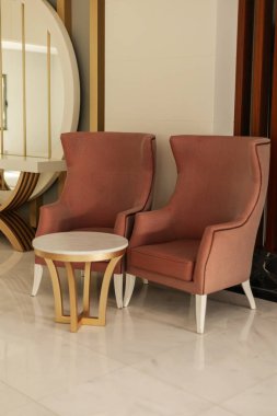 İki zarif pembe sandalye yuvarlak beyaz bir masayı kuşatarak karşılama alanı oluşturuyor. Modern dekor düz çizgiler ve parlak bir atmosfere sahiptir..