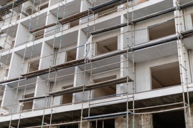 İnşaat işçileri, inşaat iskelesinin tamamlanmamış pencere çerçeveleriyle çevrili olduğu modern bir inşaat sahasında çalışıyorlar..