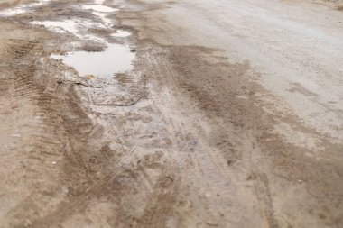 Sahne, yağmurdan sonra geride bırakılmış lastik izleri ve su birikintileriyle kaplı çamurlu bir yol gösteriyor. Araçların yıpranmasını ve hava durumunun kırsal yollardaki etkilerini yansıtıyor..