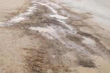 Yakın zamanda yağan yağmurdan sonra, toprak bir yol kuru toprakla çevrili su birikintilerini ve ıslak bölgeleri gösteriyor. Lastik izleri kırsal bölgedeki araç geçidini gösteriyor..
