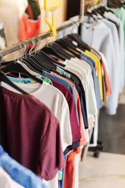 Bir perakende mağazasındaki giyim mağazasında bir dizi canlı tişört düzgünce düzenleniyor. Sıcak öğleden sonra ışığı müşteriler için mevcut her gömleğin rengini ve tarzını vurgular.