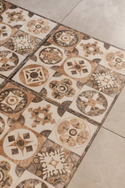 Karmaşık desenleri ve toprak renkleri olan dekoratif fayanslar, kapalı alan ortamının zeminini kaplıyor. Fayanslar, odanın estetiğini artırıyor. Sanat ve tasarım sergiliyor..