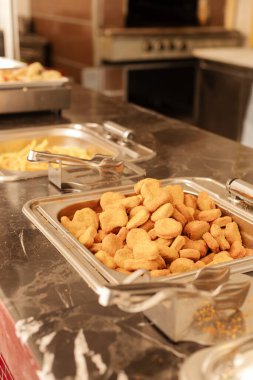 Bir servis istasyonunda altın tavuk nuggetlarıyla dolu büyük bir tepsi ve yanında başka yemekler yer alır. Sıcacık bir ortam, sıradan yemek toplantıları için mükemmel..