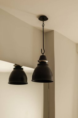 Minimalist bir ortamda tavandan sarkan iki siyah kolye, rahat bir atmosfer yaratıyor. Tasarım basit ama zarif, odanın dekorunu geliştiriyor..
