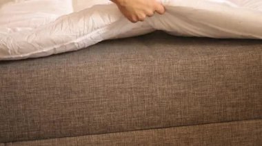 Bir insan kanepeye bir şilte yerleştirir. Gece kanepede uyumaya hazırlanıyorlar. Oturma odası dinlenmek için hazırlandı..