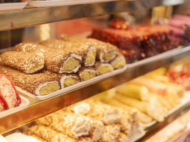 Renkli tatlılar raflarda güzelce düzenlenir. Müşteriler pastalar ve pastalar da dahil olmak üzere farklı tatlılar görebilirler. Dükkan aydınlık ve meşgul..