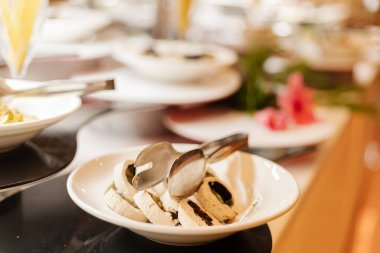 Tabaklar açık büfede çeşitli yiyecek öğeleri bulundurur. Maşa bir kase dilimlenmiş peynirin içinde dinleniyor. Diğer tabaklar daha fazla yiyecek seçeneğiyle yakınlarda düzenlenmiştir..