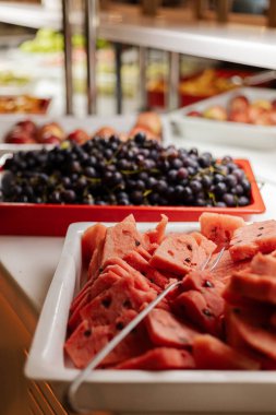 Misafirler çeşitli taze meyveler seçebilirler. Dilimlenmiş karpuz ve büfe masasındaki üzümler de dahil. Ayar aydınlık, yemekler için davetkar bir ortam yaratıyor..