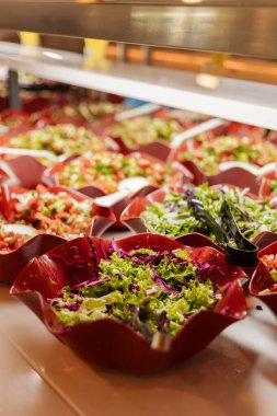 Açık büfede taze yeşillik ve malzemelerle çeşitli salatalar düzenlenir. İnsanlar öğle yemeği için farklı seçenekler seçebilirler. Aydınlık ve yoğun bir ortam..