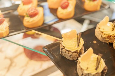 Küçük tatlılar bir pastanenin cam vitrinine yerleştiriliyor. Şekerlemeler arasında krema ve malzemeler var. Bu da müşteriler için görsel olarak cazip hale getiriyor..