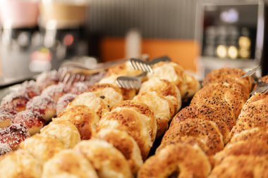 Bir fırında taze ekmek ve hamur işi seçimi sergileniyor. Farklı türde rulo ve tatlılar tepsilerde düzgün bir şekilde düzenlenir ve müşterileri seçmeye davet edilir..