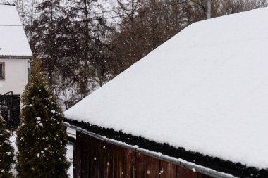 Kar, yerleşim alanındaki bir çatıyı ve yakınlardaki ağaçları kaplıyor. Kar taneleri sürekli düşüyor, bu da soğuk bir kış günü olduğunu gösteriyor. Sahne basit bir kış manzarasını gösteriyor..